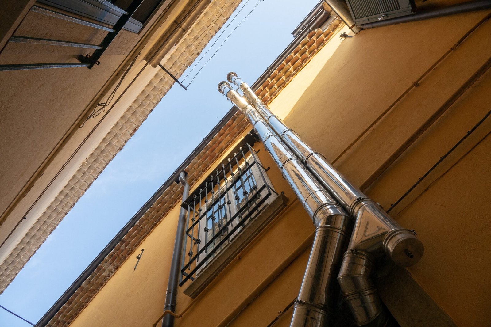 A low angle shot of two pipes as they go up the building next to a window